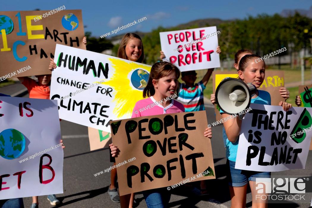 Stock Photo: Front view of a diverse group of elementary school pupils walking down a road in the sun on a protest march, carrying signs with environmental and conservation.