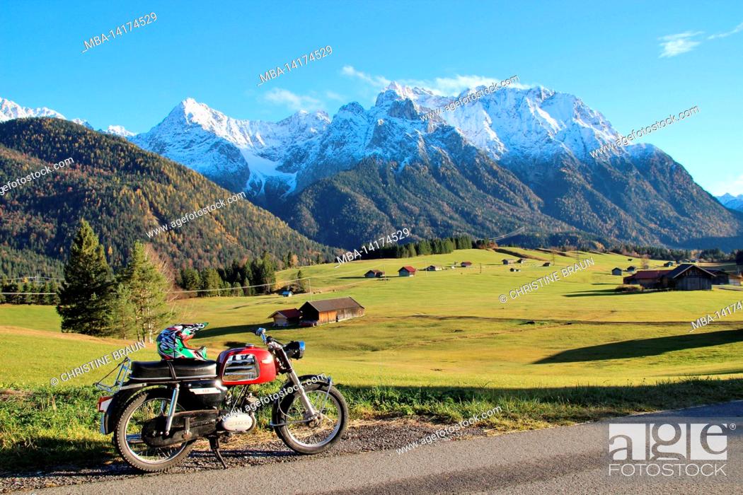 Stock Photo: A motorcycle stands on a field path between Krün and Mittenwald in front of the alpine backdrop of the freshly snow-covered Karwendel Mountains.