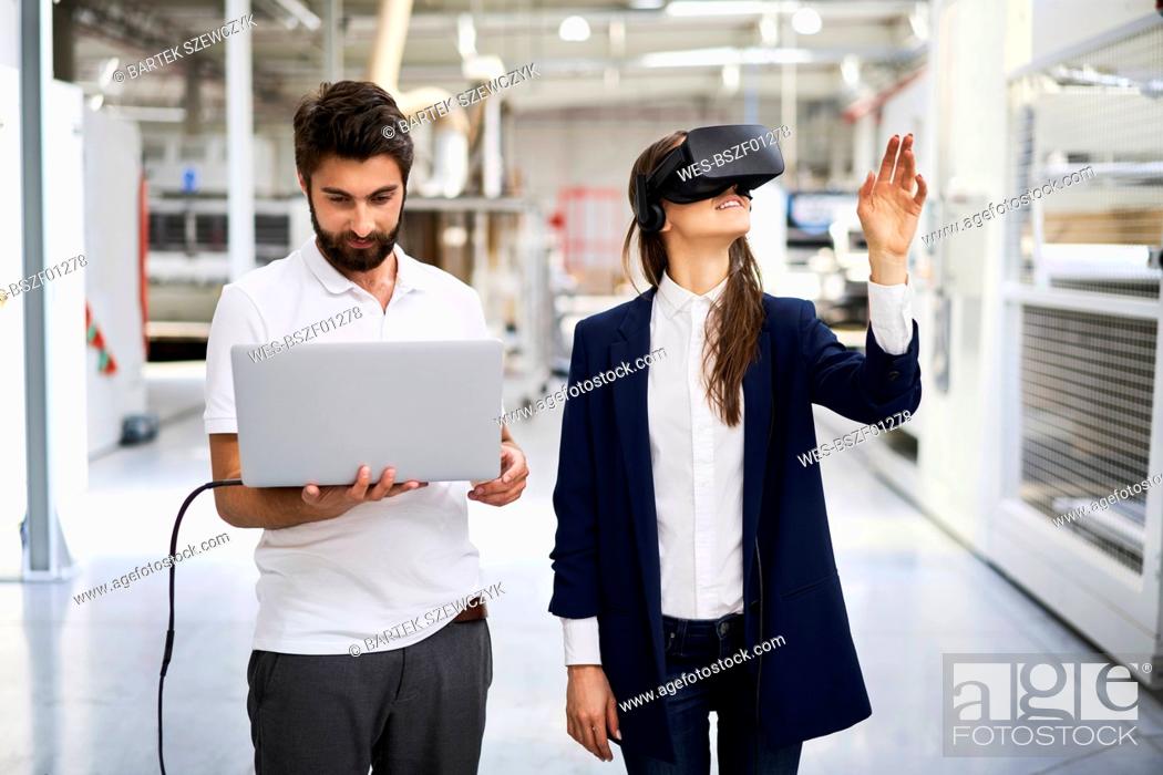 Stock Photo: Man with laptop and businesswoman wearing VR glasses in factory.