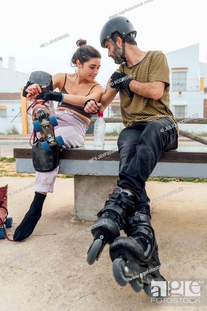 Stock Photo: Young woman looking at man's tattoo while sitting on bench with roller skates.
