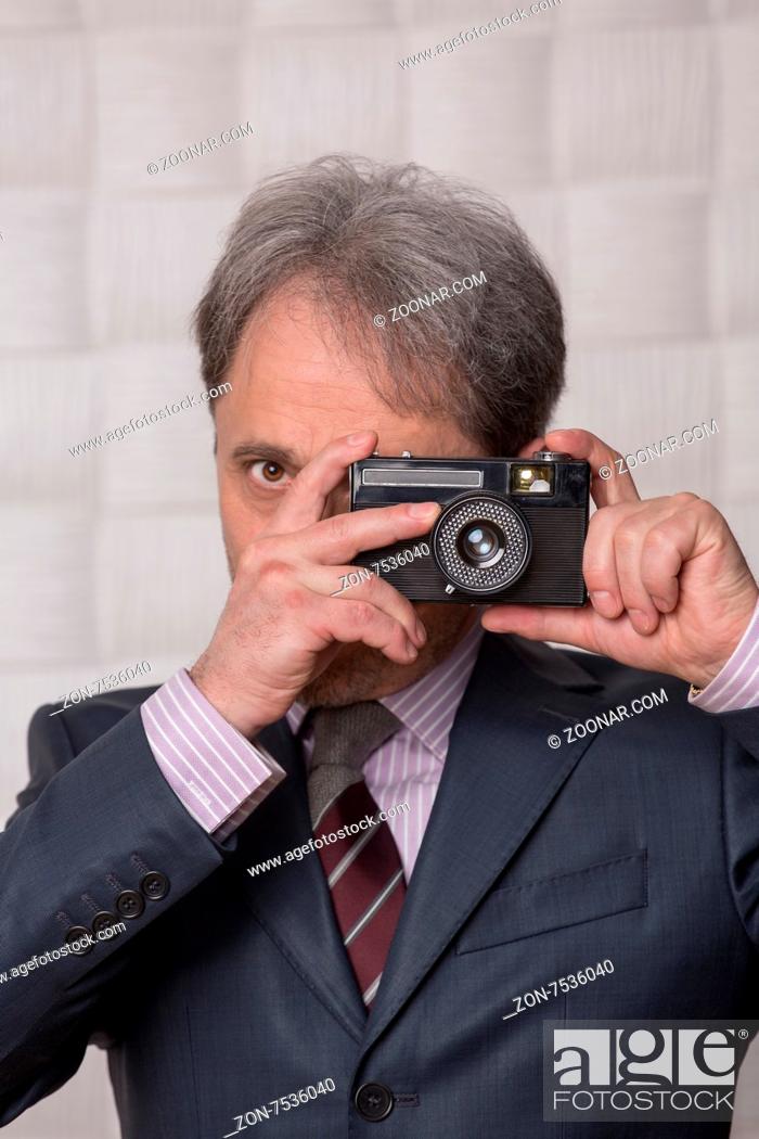 Stock Photo: Businessman making different pictures. Mature man in business suit happy focusing on photographer isolated on cream bcakground.
