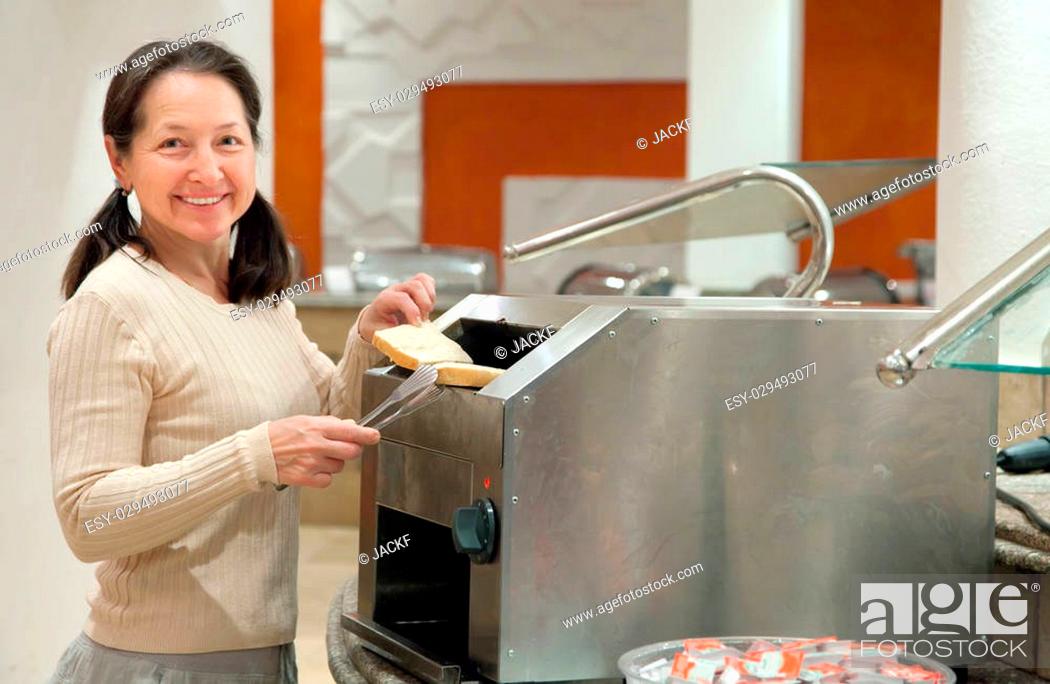 Stock Photo: woman makes toast in a toaster at hotel restaurant.