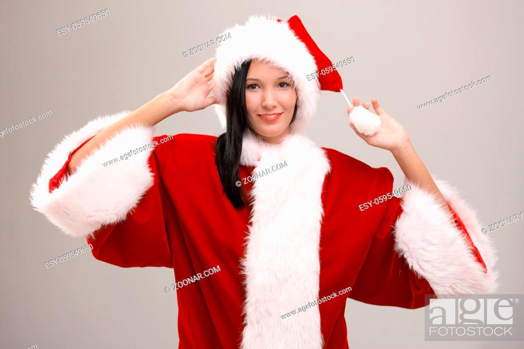 Stock Photo: Cheerful young woman wearing huge Santa Claus costume, looking at camera, isolated on gray background.