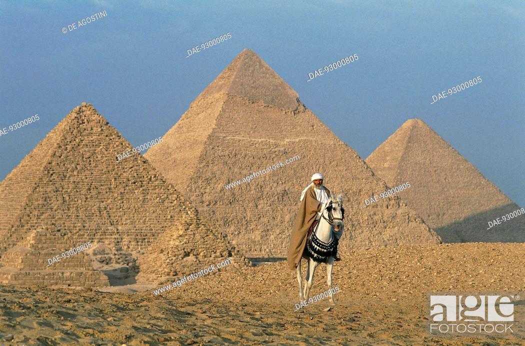 Stock Photo: A bedouin on horseback, with the pyramids of Cheops, Chephren and Menkaure in the background, Giza Plateau (UNESCO World Heritage List, 1979), Egypt.