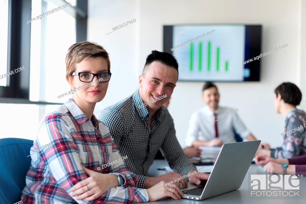 Stock Photo: young startup business people, couple working on laptop computer, businesspeople group on meeting in background at office interior.