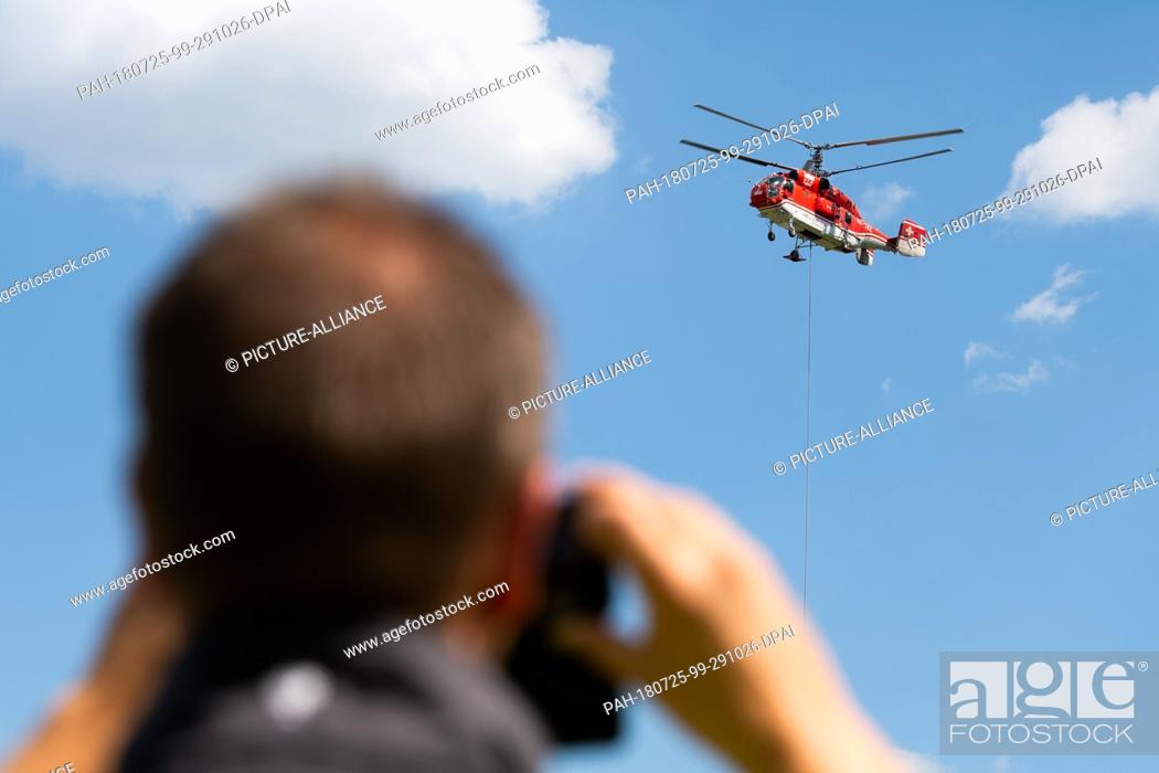 Stock Photo: 25 July 2018, Willingen, Germany: A spectator takes a photograph of a heavy-duty helicopter with which the last parts of the new 8-seater chairlift ""K1.