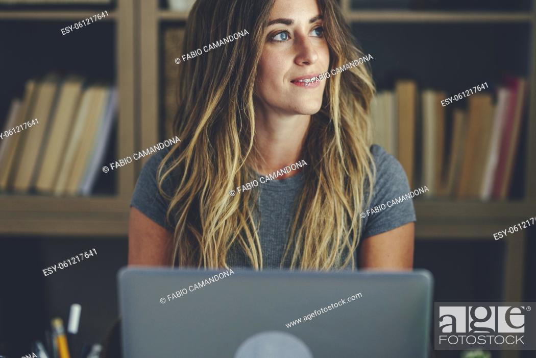 Stock Photo: Attractive smiling young woman looking away using laptop while sitting at home, Beautiful woman using laptop. Thoughtful girl browsing social media content or.