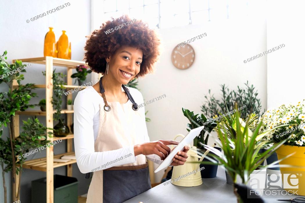 Stock Photo: Smiling female florist holding digital tablet by potted plants at store.