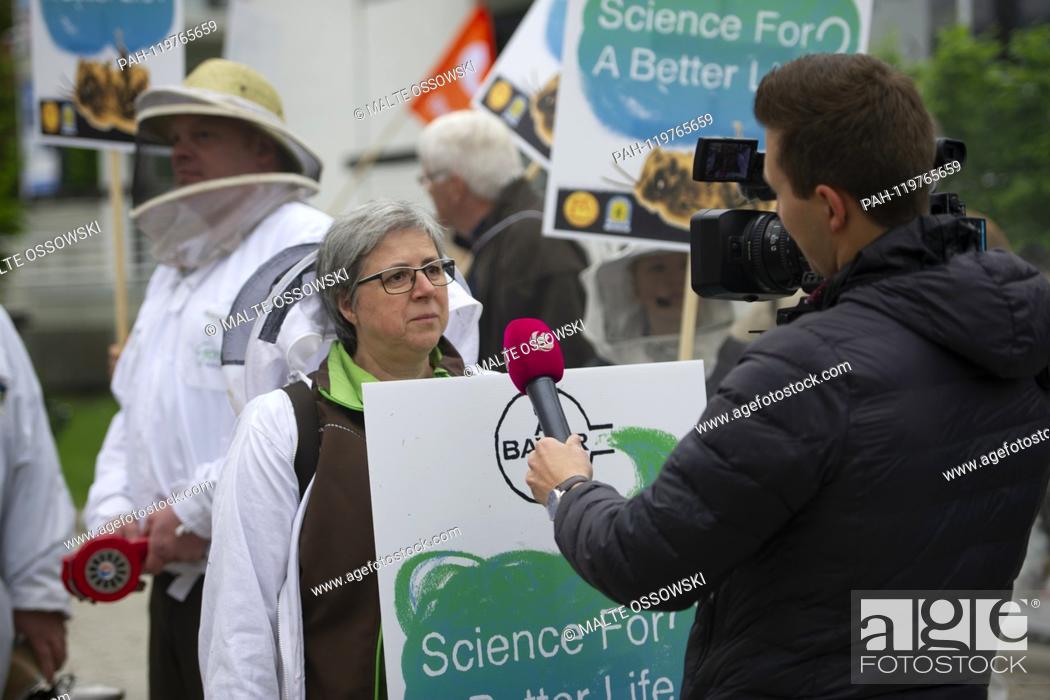 Stock Photo: A camera team interviews a beekeeper, activists protest versus the merger of Bayer and Monsanto, versus glyphosate, farmers versus seed patents and arable.