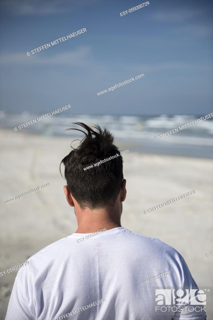 Photo de stock: Close-up of head, neck and shoulders of a man seen from behind walking on the beach with wind blowing hair into a humorous point on top of his head.
