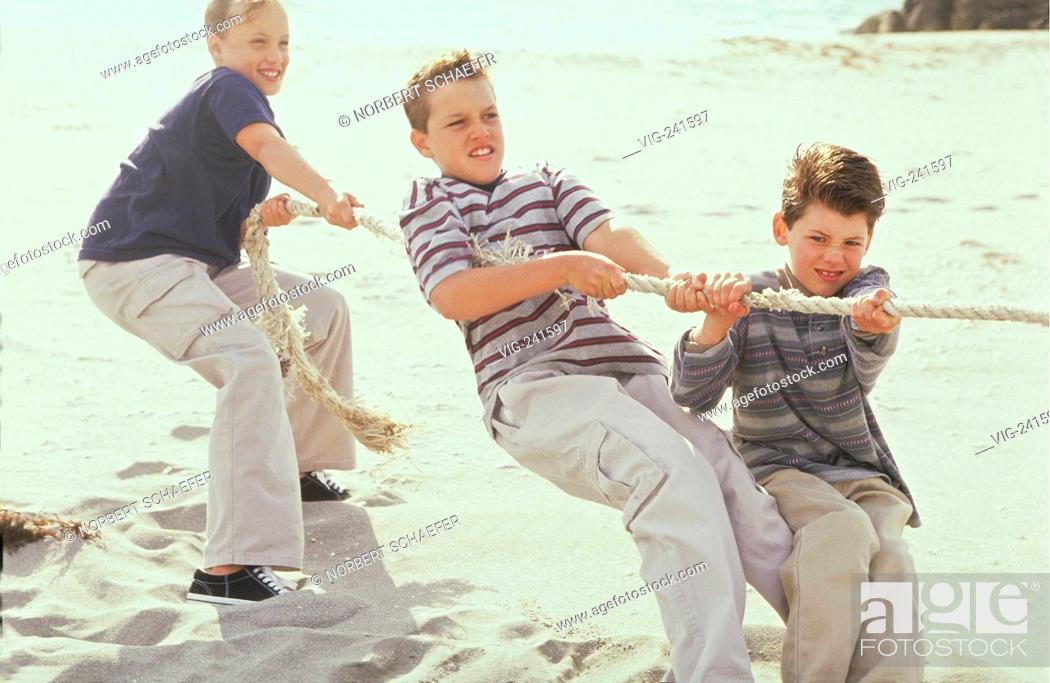 Photo de stock: beachscene, portrait, blond girl and 2 boys in the age of 10-12 years pulling the rope in the sand  - GERMANY, 22/04/2004.