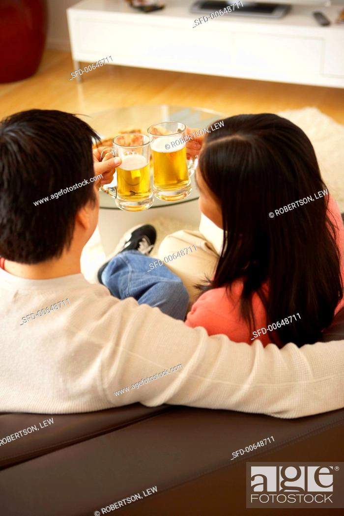 Stock Photo: Couple on sofa clinking glasses of beer.