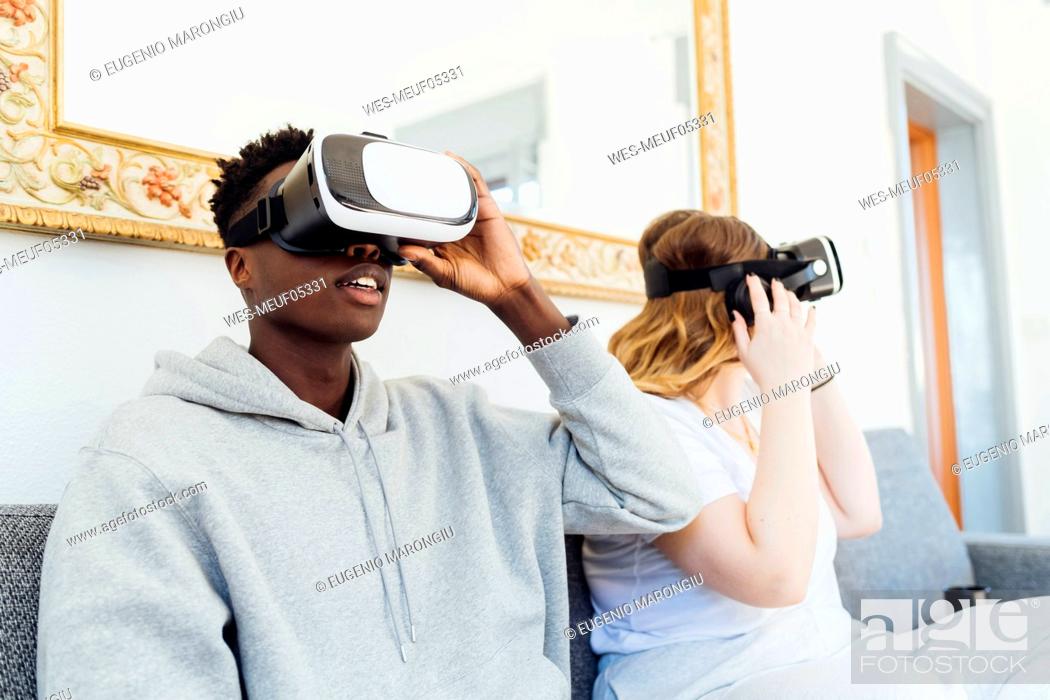 Photo de stock: Young couple wearing virtual reality simulators sitting on sofa at home.