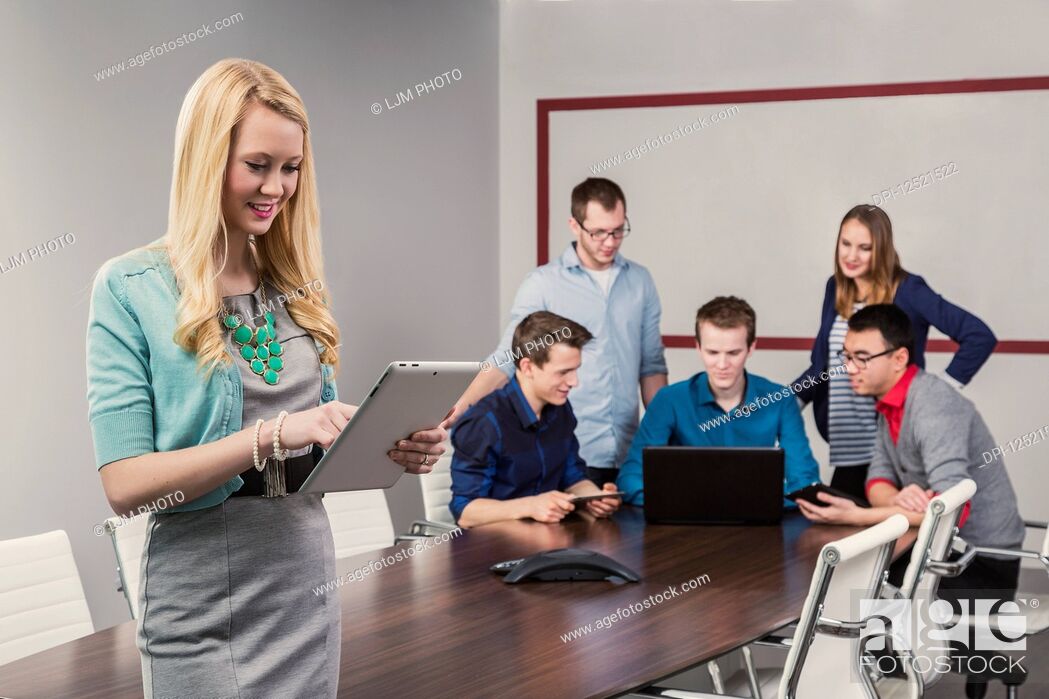 Stock Photo: A beautiful young millennial business woman working on her tablet in a conference room with her co-workers; Sherwood Park, Alberta, Canada.
