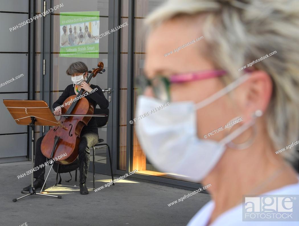 Stock Photo: 23 April 2020, Brandenburg, Cottbus: A musician from the Cottbus State Theatre plays for patients in front of the main entrance to the Carl-Thiem-Klinikum (CTK).