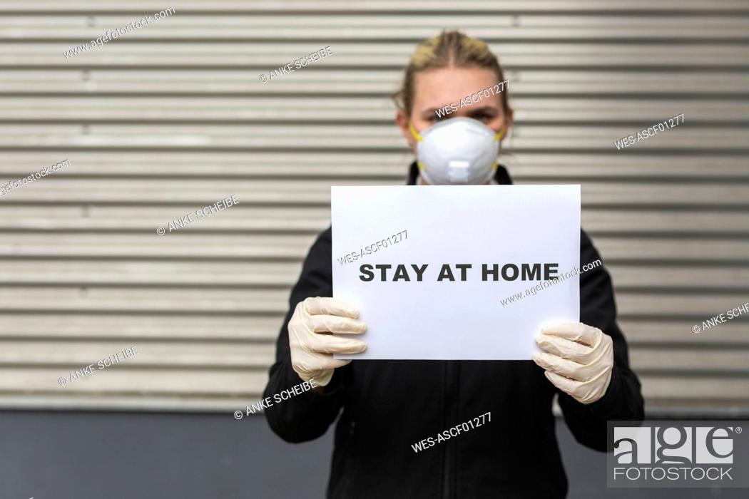 Stock Photo: Teenage girl wearing protective mask and gloves holding sign with request 'Stay At Home'.