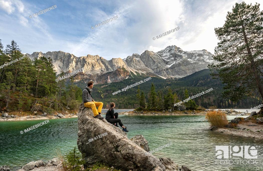 Stock Photo: Young woman and young man sitting on a rock at the shore, view into the distance, Eibsee lake in front of Zugspitzmassiv with Zugspitze, Wetterstein Mountains.