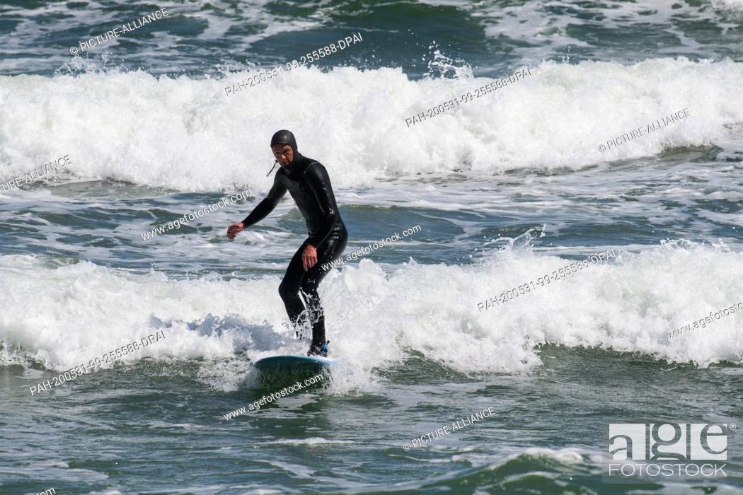 Stock Photo: 31 May 2020, Mecklenburg-Western Pomerania, Binz: Nils Miller jumps with his surfboard over waves in the Baltic Sea. Lively northeast wind has brought joy to.