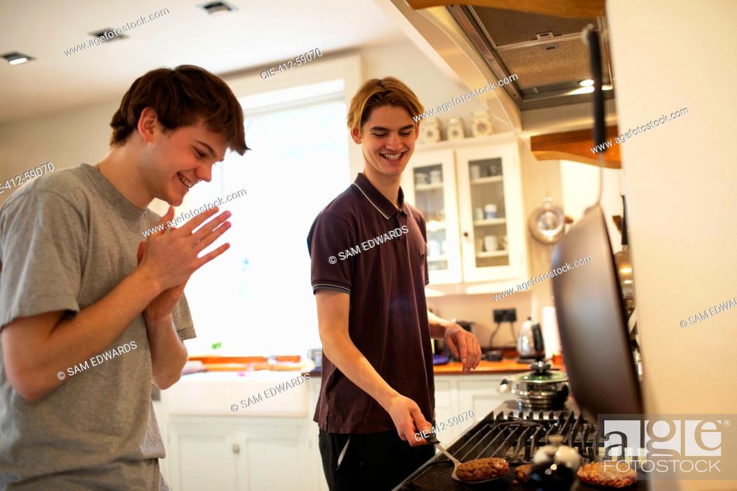 Stock Photo: Happy teenage boys grilling hamburgers at kitchen stove.