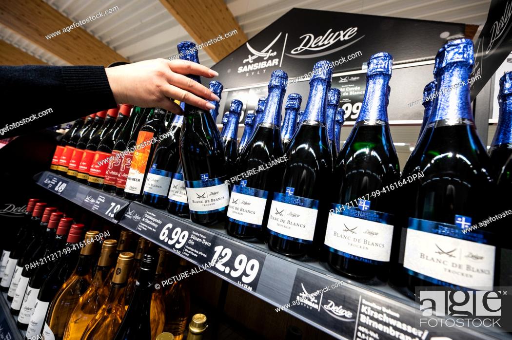 Stock Photo: PRODUCTION - 15 December 2021, North Rhine-Westphalia, Kaarst: A woman takes a bottle of Blanc de Blancs from the shelf with Sansibar and deluxe products in a.