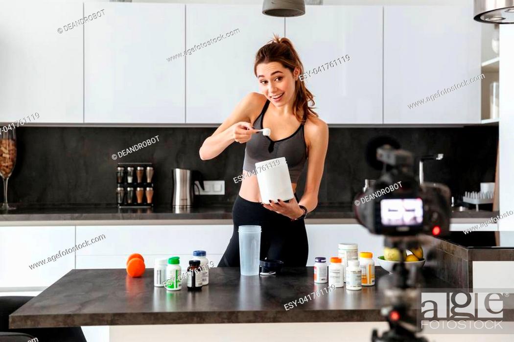 Stock Photo: Happy healthy young girl recording her video blog episode about healthy food additives while standing at the kitchen at home.