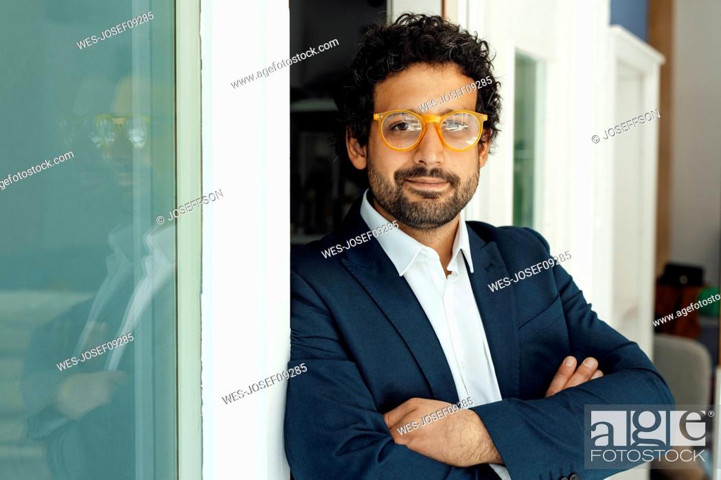 Stock Photo: Smiling businessman wearing eyeglasses standing with arms crossed at doorway.