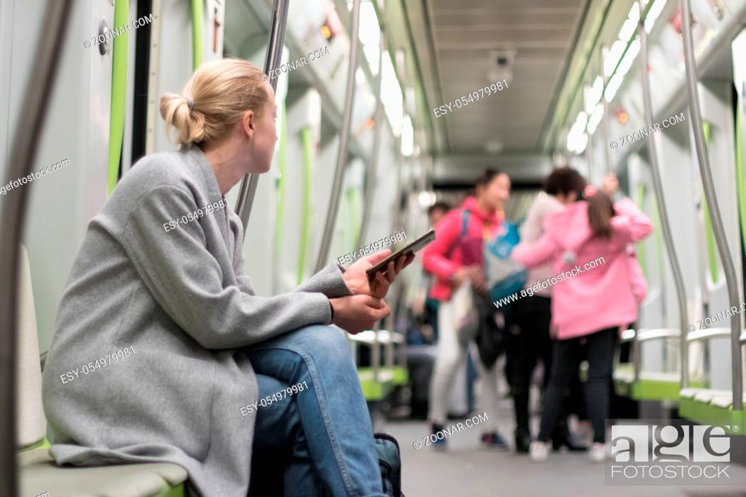 Stock Photo: Beautiful blonde caucasian woman wearing winter coat and jeans using smart phone while traveling by metro. Public transportation concept.