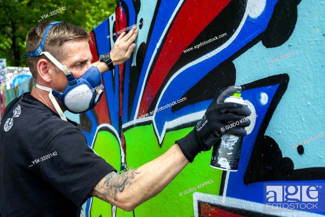 Stock Photo: Berlin, Germany. Graffity artist creating jet another piece of urban art on parts of the former Berlin Wall, bordering former East-Germany or DDR.