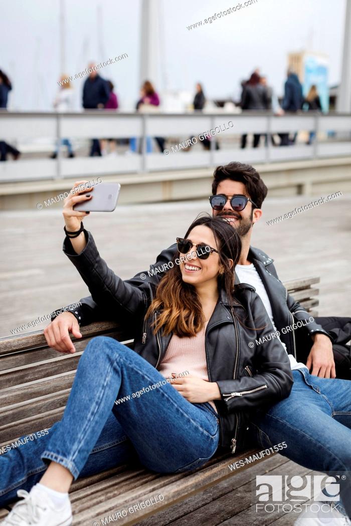 Stock Photo: Spain, Barcelona, happy young couple resting on a bench taking a selfie.