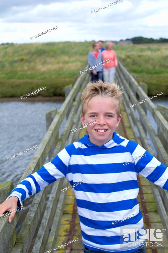 Stock Photo: Portrait of a young boy on a bridge with his family in the background. He is smiling at the camera and wearing casual clothing.