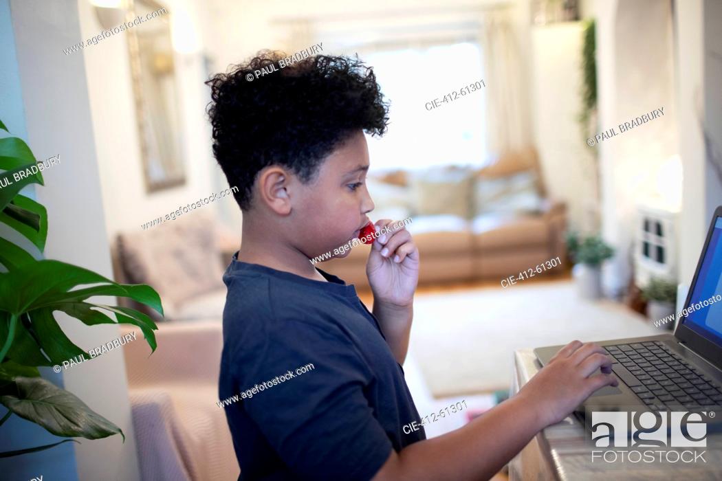 Stock Photo: Boy eating strawberries at laptop at home.