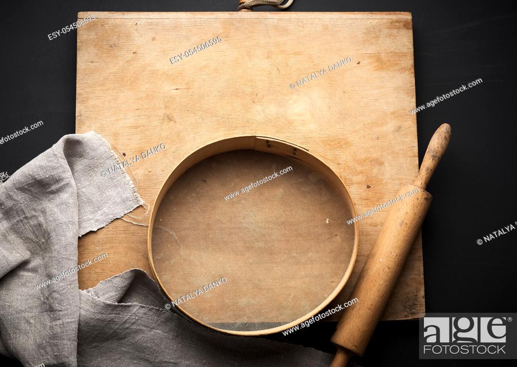 Stock Photo: vintage wooden rolling pin and a round sieve, gray linen napkin, black table, top view, cooking utensils for making dough.