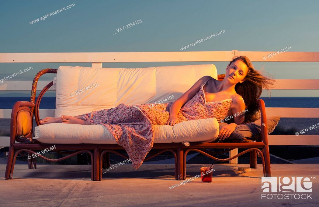 Stock Photo: A Young Woman Poses On A Couch On An Outdoor Patio With The Ocean In The Background; Tarifa, Cadiz, Andalusia, Spain.