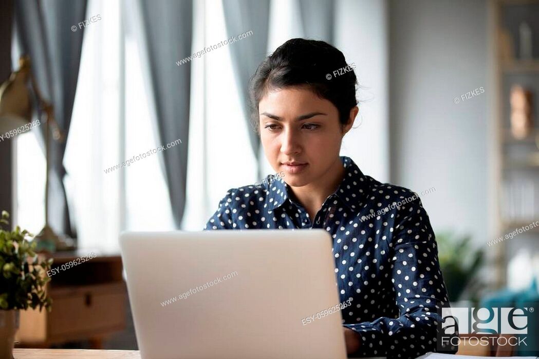Stock Photo: Serious Indian woman working on laptop, focused young businesswoman looking at screen, reading important news in email, writing message.