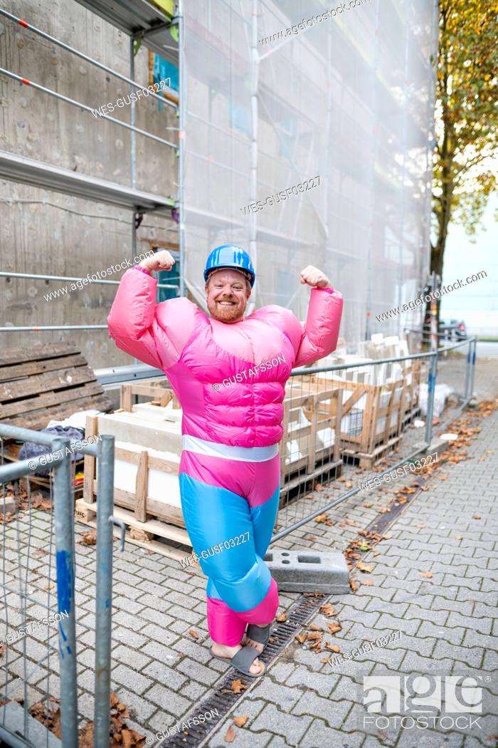 Stock Photo: Portrait of a proud man wearing pink bodybuilder costume and hard hat at construction site.