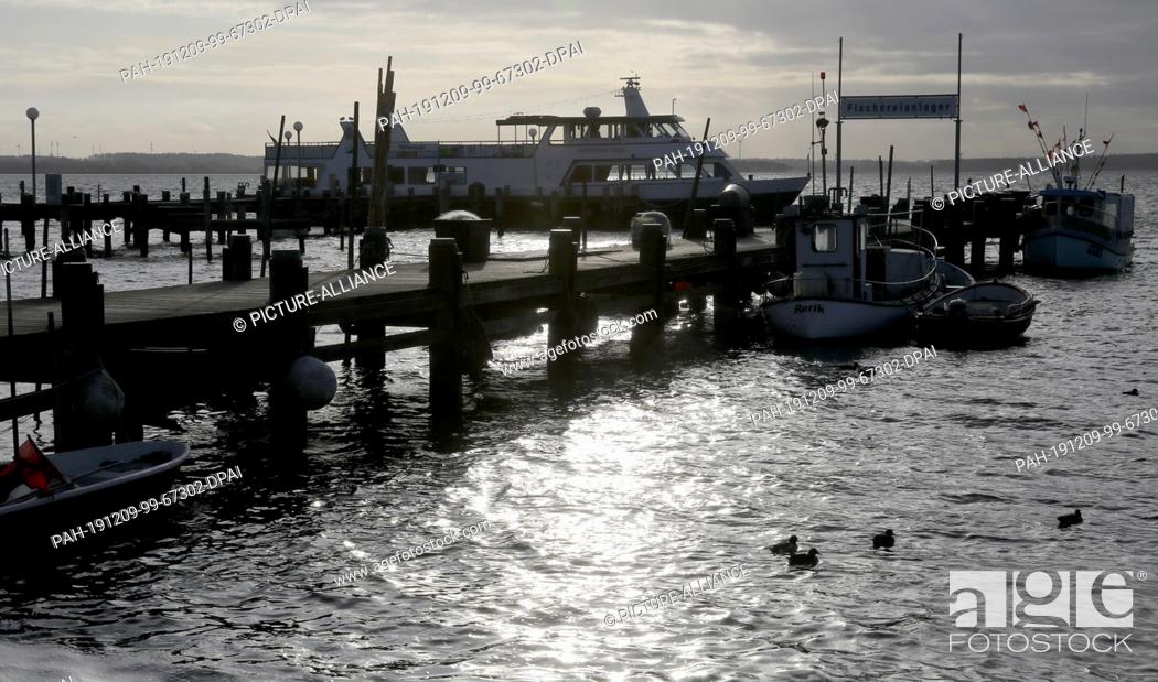 Stock Photo: 09 December 2019, Mecklenburg-Western Pomerania, Rerik: The sunlight reflects in the harbour at the Salzhaff in the water, in the background dark clouds pass by.