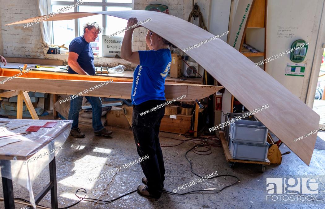 Stock Photo: 19 May 2022, Mecklenburg-Western Pomerania, Peenemünde: Boat builder Ursula Latus brings a plywood plate for the further construction of a canoe two-seater at.