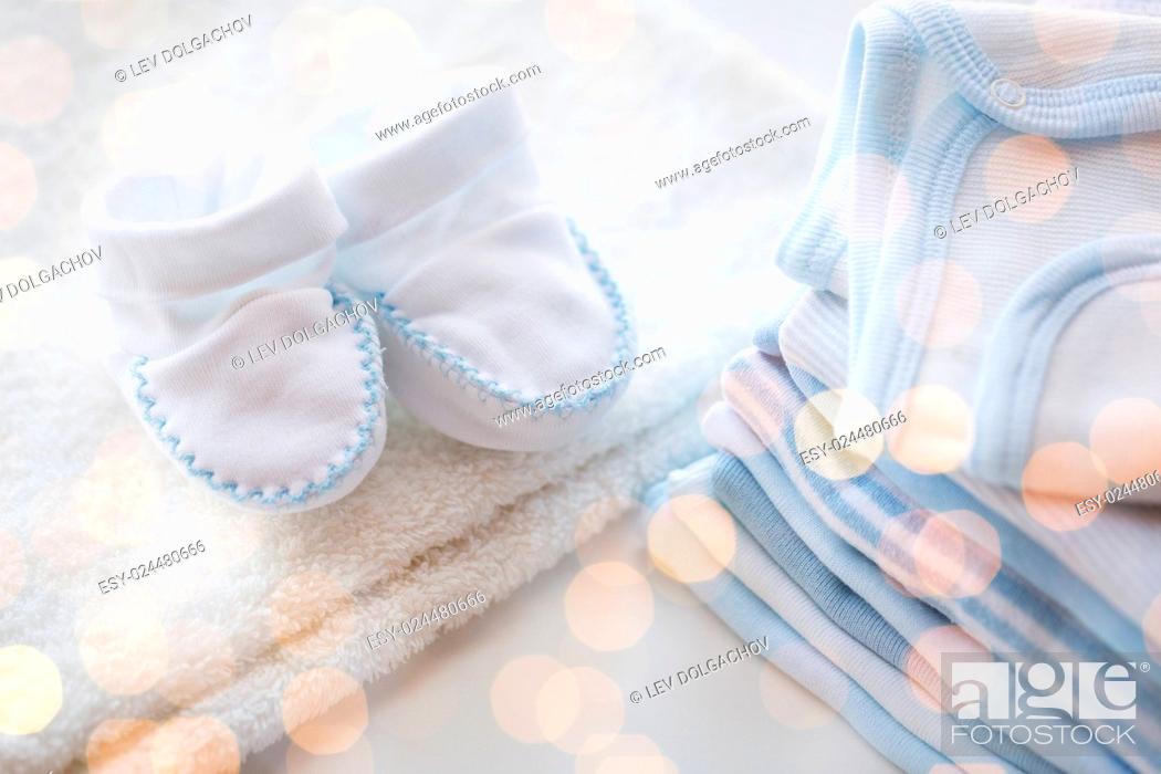 Stock Photo: clothing, babyhood, motherhood and object concept - close up of white baby bootees with pile of clothes for newborn boy.