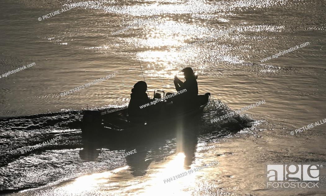 Stock Photo: 22 March 2021, Brandenburg, Frankfurt (Oder): Two anglers are sailing upstream in a motorboat in the light of the morning sun on the German-Polish border river.