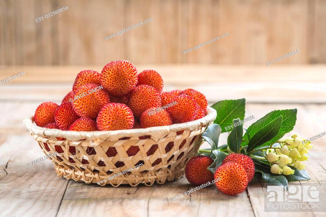 Stock Photo: Basket with ripe arbutus unedo fruits, leaves and floers on a wooden background.