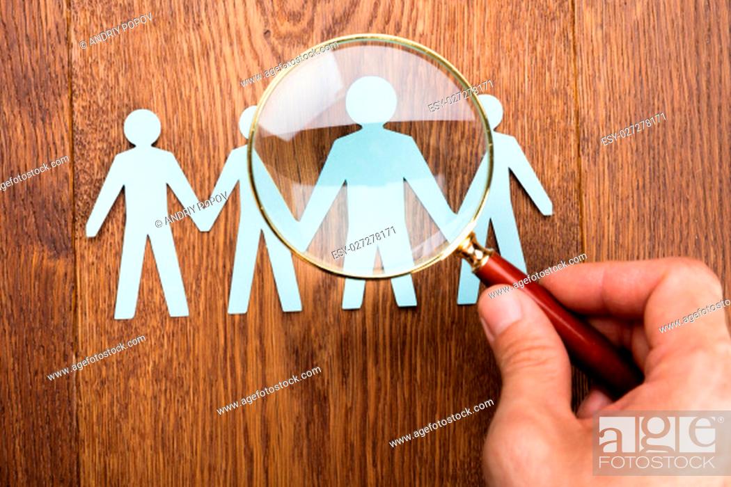 Stock Photo: High Angle View Of Person Using Magnifying Glass On Papercut At Wooden Desk.
