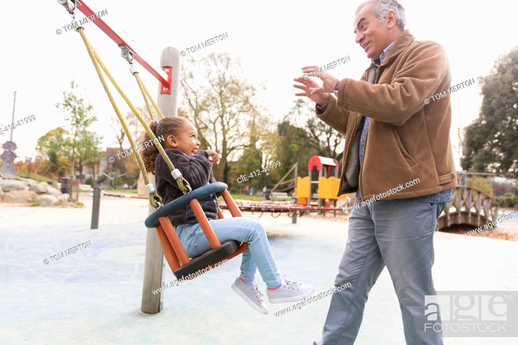 Photo de stock: Grandfather pushing granddaughter on playground swing.