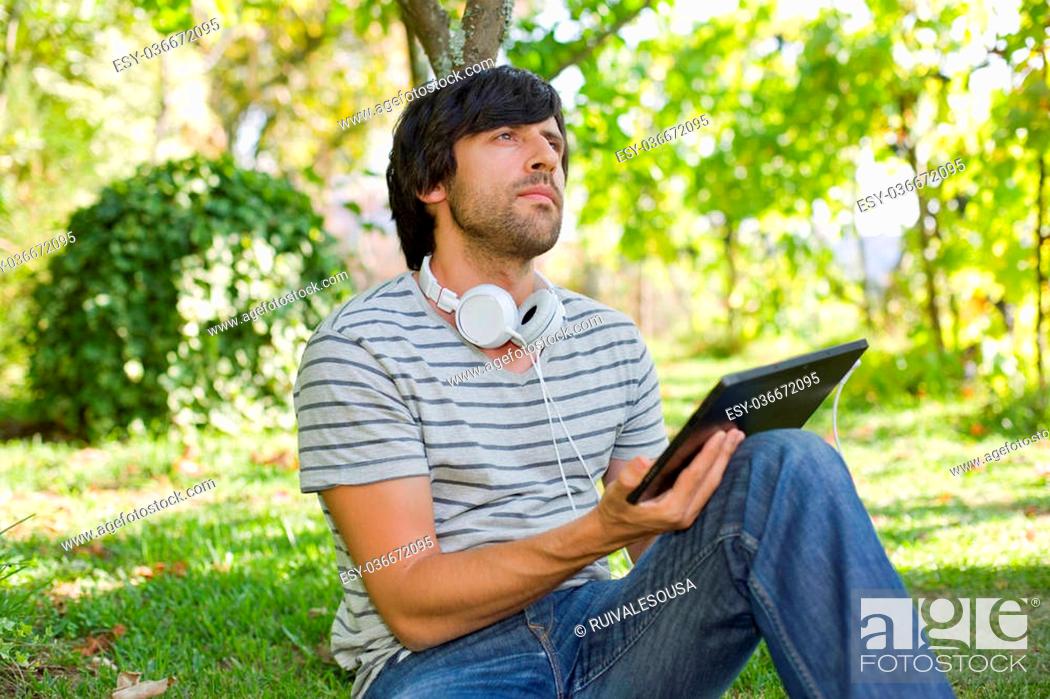 Stock Photo: young man relaxing with a tablet pc listening music with headphones on a the park, outdoor.