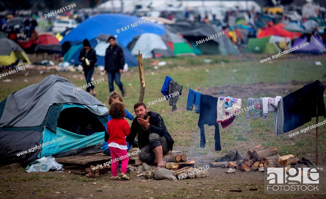 Stock Photo: A man with two children sitting in front of his tent in the refugee camp in Idomeni, Greece, 11 March 2016. Since the border was closed down, 12.