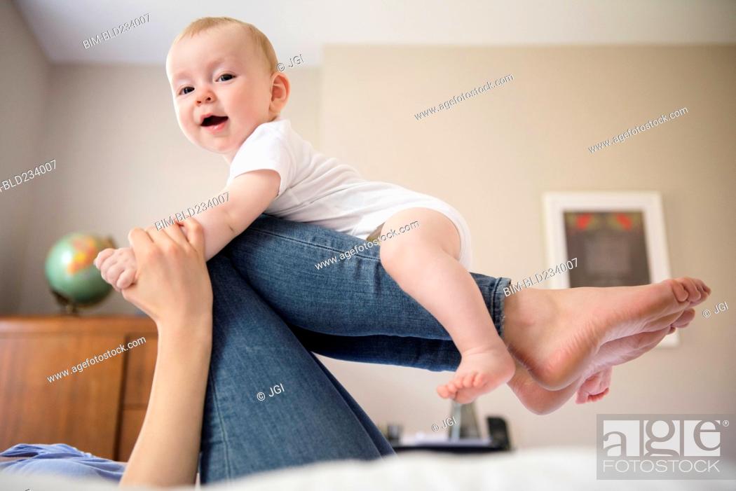Stock Photo: Caucasian mother laying on bed balancing baby son on legs.