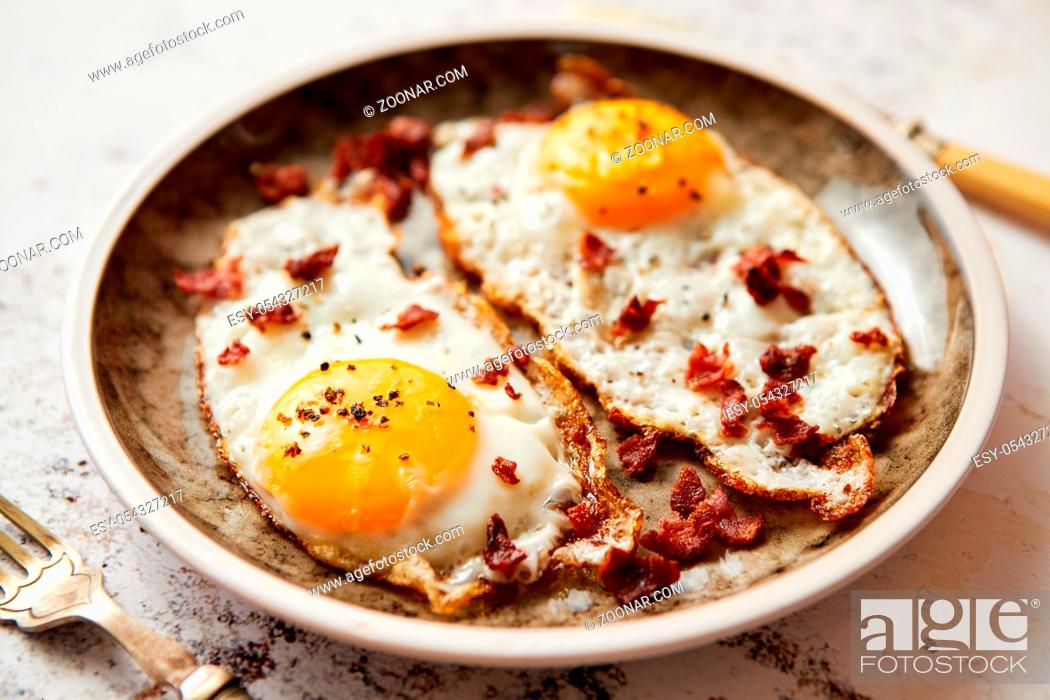 Stock Photo: Two fresh fried eggs with crunchy crisp bacon served on rustic plate. Fork and knife on sides. Top view.