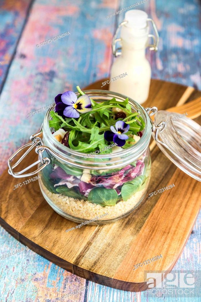 Stock Photo: A quinoa salad with lambs lettuce, radicchio, rocket, croutons, goat's cheese and horned violets in a glass jar on a wooden board.