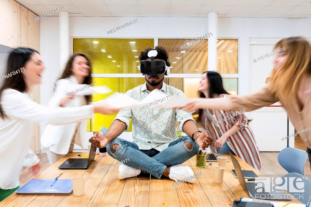 Stock Photo: Businessman sitting on desk in conference room in office wearing VR goggles.