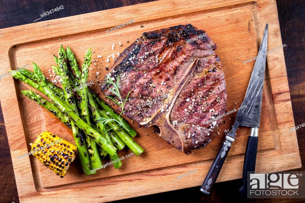 Imagen: Barbecue dry aged Wagyu Porterhouse Steak with green Asparagus as close-up on a cutting board.