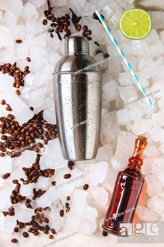 Stock Photo: Coffe cocktail frappe making concept. Silver shaker, coffee beans, dark rum, sliced lime, cocktail tube over crushed ice cubes. Flat lay, space.